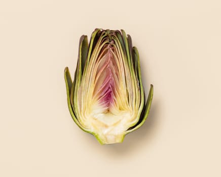 Cut raw purple artichoke on light yellow background top view. Fresh vegetables from farmers market ready to cook, vegetarian diet. Italian cousine ingredient