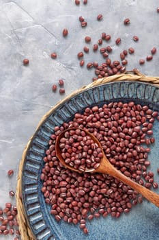 Ceramic blue plate full of dried red azuki beans with a wooden spoon on grey table top view, copy space. Healthy vegetarian food, legumes protein source. Traditional East Asian cousin ingredient