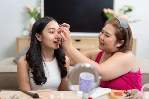 Two friends joyfully apply makeup to each other, highlighting their connection through shared creativity and fun in a welcoming environment.