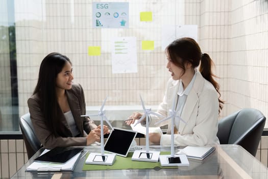 Two women share ideas and insights regarding ESG strategies, examining models of wind energy to enhance sustainability efforts in their company.