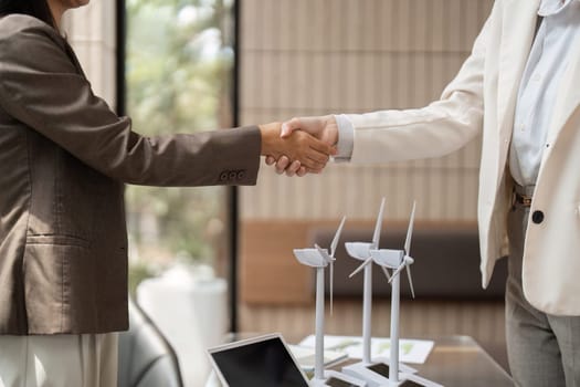 A handshake between two individuals symbolizes a partnership focused on sustainable energy initiatives. Wind turbine models in the background emphasize commitment to ESG principles.