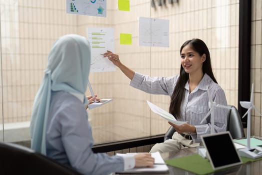Two professionals collaborate at a meeting, examining sustainable data and green energy models while strategizing for their company ESG objectives.