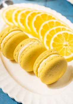 Vibrant yellow lemon macarons arranged on a white plate, accompanied by freshly sliced lemons, creating a visually appealing dessert presentation