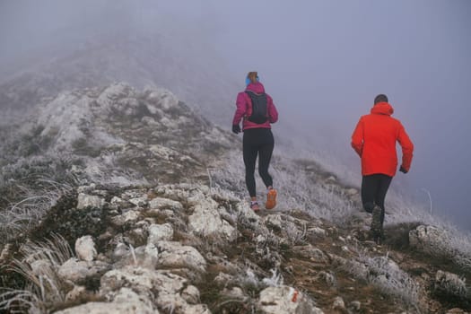 Trail running couple man and woman running on a mountain path. A couple on cross country run in early morning.