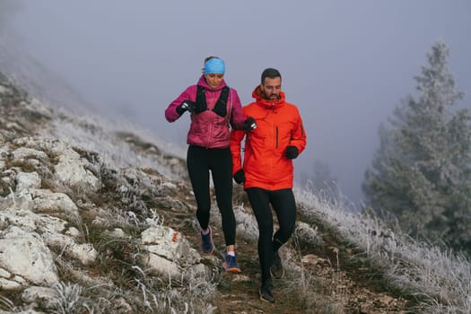 Trail running couple man and woman running on a mountain path. A couple on cross country run in early morning.