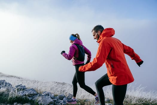 Trail running couple man and woman running on a mountain path. A couple on cross country run in early morning.