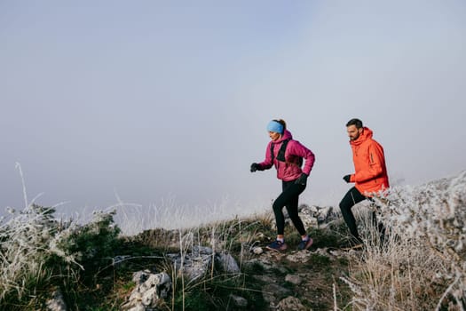 Trail running couple man and woman running on a mountain path. A couple on cross country run in early morning.