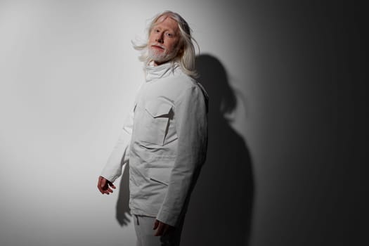 Portrait of an elderly man with long white hair in a stylish white outfit, posing against a minimalistic gradient gray background, showcasing an artistic and modern aesthetic