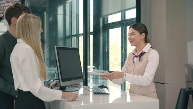 Happy Caucasian young couple check in counter desk at international airport and woman staff worker receiving boarding passes to while checking in for flight