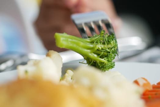 A fork lifts a piece of broccoli from a plate filled with vegetables.