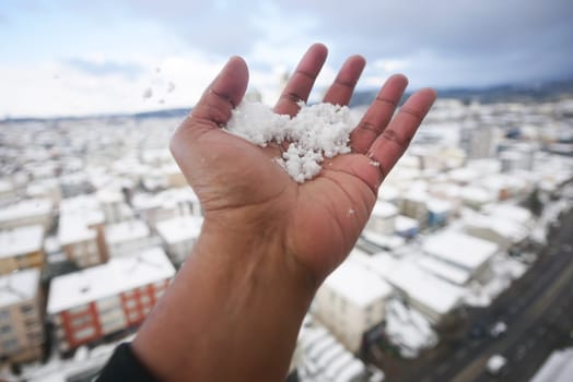 A hand offers fresh snow against a snowy urban background.