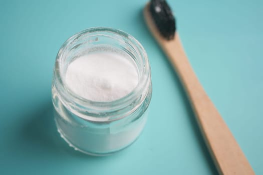 Baking soda in a jar by a bamboo toothbrush on a turquoise background.