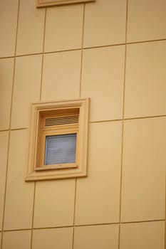A small window is framed in wood against a vibrant yellow wall.