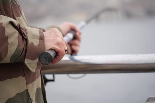 Fisherman grips fishing rod while standing on a pier.