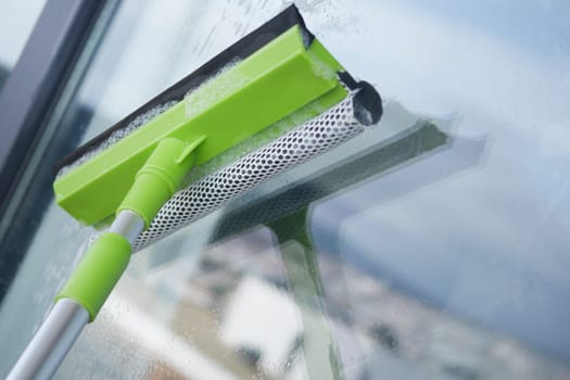 Cleaning a window with a squeegee on a sunny day, revealing clear views.