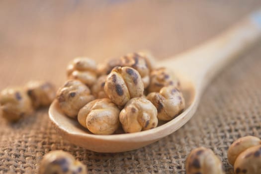 Crunchy roasted chickpeas rest in a wooden spoon on burlap fabric.