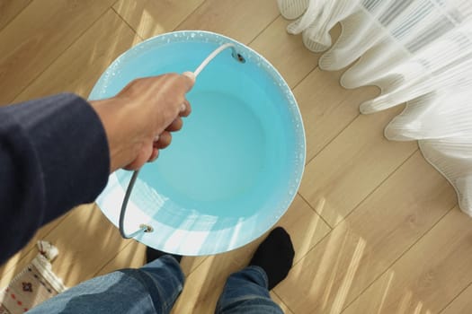 A person grips a blue bucket filled with clear water in a bright room.