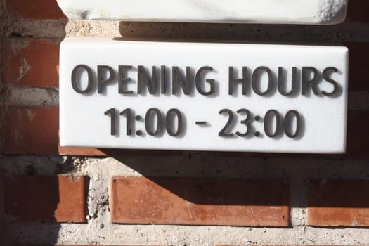 Sign showing opening hours from 11 AM to 11 PM in a brick setting.