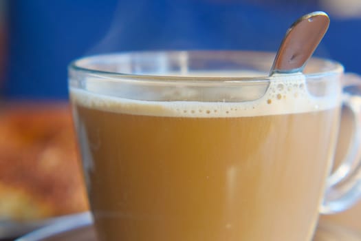 A freshly brewed drink sits in a glass cup with steam rising gently.