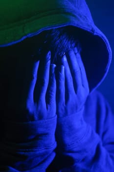 A person covers their face in distress under blue lighting at night.