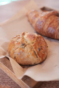 A rustic wooden tray holds freshly baked bread rolls and croissants.