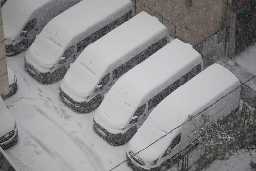 Several vans are completely buried in snow during a winter storm.