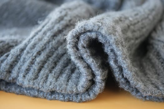 Soft gray wool sweater is neatly rolled on a light wooden surface.