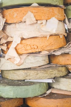 Various cheese wheels in different colors are stacked high together.