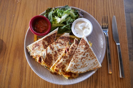 Quesadilla with salad and sauces presented on a plate at lunch.