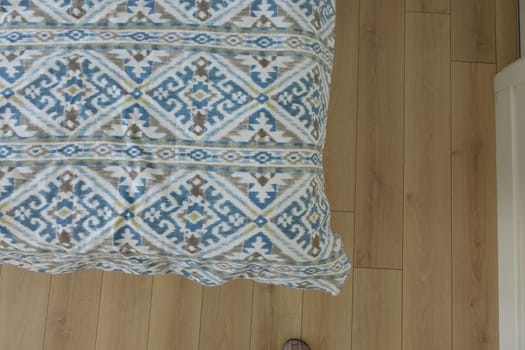 A cozy blanket with an intricate design rests on a light wooden floor.
