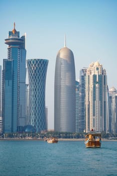 Traditional wooden boats float in the water by a modern city skyline.