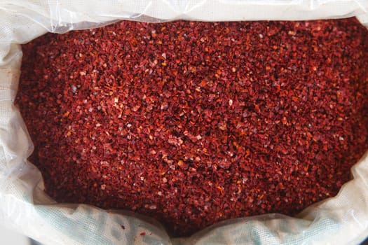Bright red spices fill a burlap sack at a bustling market stand.