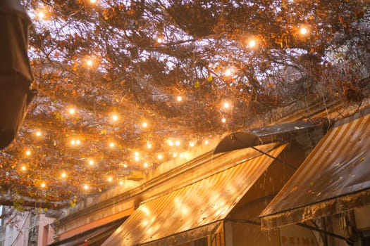 Warm lights illuminate a quaint alley as rain falls on charming cafes.
