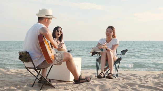 Happy friend have fun playing guitar and clap in camp they smiling together in holiday on sand beach near camping tent vacation time at sunset, Young Asian group woman and man in summer travel outdoor