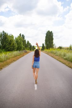 Attractive girl, stands posing, hands up in the middle of an asphalt road near the field, copies space for content.