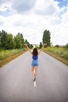Attractive girl, stands posing, hands up in the middle of an asphalt road near the field, copies space for content