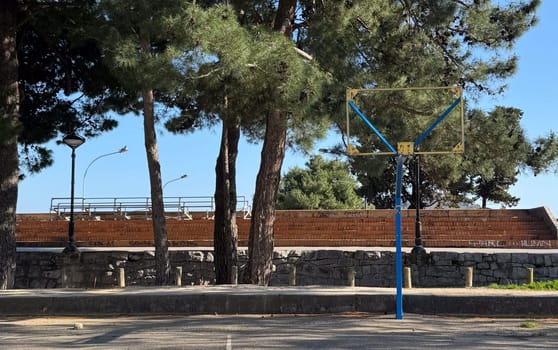 Budva,Montenegro-April 11,2025:A weathered basketball hoop stands alone in a tree-lined area with graffiti-covered steps in the background. High quality photo