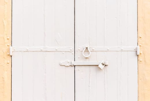 Closed vintage garage gates made of wooden palnks and an iron lock on it painted in beige and ochre colors.