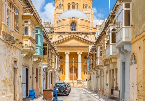View of the Basilica of Christ the King in Paola through a narrow street with traditional Maltese houses, Tarxien, Malta.