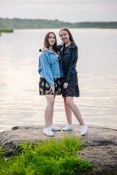 Female friends embracing on lakeside boulder, sharing warm moment of connection during outdoor adventure