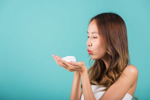 Portrait Asian young woman hands are adorned with white foam mousse and she blowing studio shot isolated on blue background, beautiful female holding and blow cleansing foam, beauty skincare