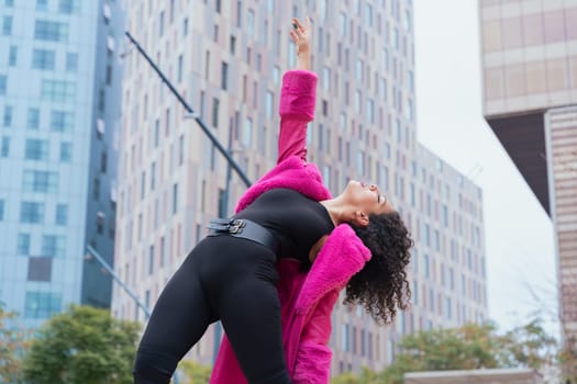 African american dancer with curly hair wearing a pink coat, expressing movement and energy in an urban environment. Modern fashion, contemporary dance,and artistic performance against a city backdrop