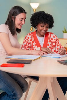 Caucasian and African American students work together using a laptop and notebook. Focused and cheerful, they collaborate in a cozy indoor space, representing learning, diversity, and teamwork.