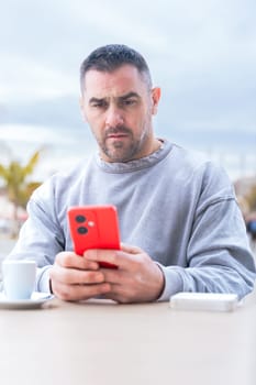 serious caucasian man, serious man looking at her mobile smart phone, typing a message on the terrace of an outdoor cafe. Addiction to social networks. App, device technology concept.vertical