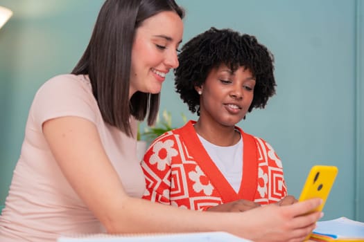 Caucasian and African American friends share a joyful moment as they look at a mobile phone together. Their smiles and relaxed vibe highlight connection, friendship, and digital engagement indoors.