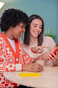 Caucasian and African American friends share a joyful moment as they look at a mobile phone together. Their smiles and relaxed vibe highlight connection, friendship, and digital engagement indoors.
