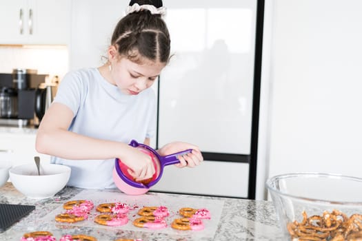 With focused attention, this budding culinary artist dips pretzels into a pot of melted chocolate, creating sweet delights in the warmth of a well-lit home kitchen.