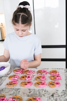 With focused attention, this budding culinary artist dips pretzels into a pot of melted chocolate, creating sweet delights in the warmth of a well-lit home kitchen.