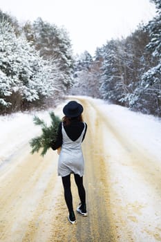 A girl in a dress and hat stands with her back in the middle of a winter road in the forest