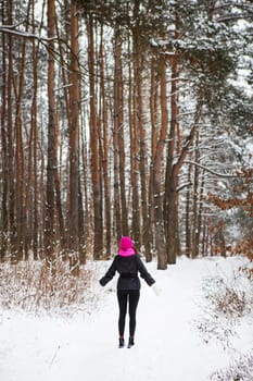 A girl in a pink scarf and hat stands in the middle of a pine forest. Beautiful pine forest on a frosty day